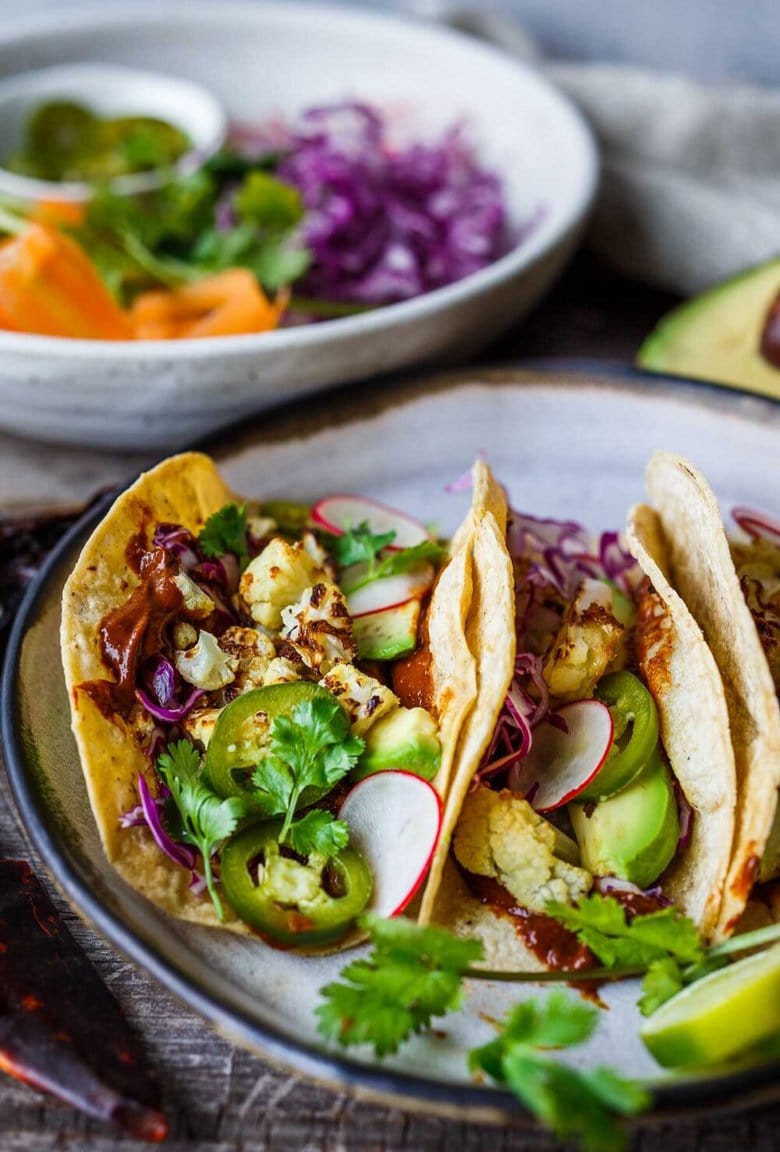 烤花椰菜炸玉米饼和快速简便的摩尔rojo酱！ These healthy vegan tacos are loaded up with cabbage, avocado, radishes and cilantro and full of satisfying flavor and fresh crunchy ingredients.